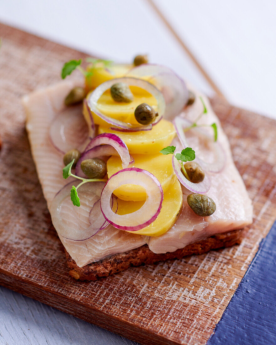 A slice of bread topped with herring, potatoes and capers