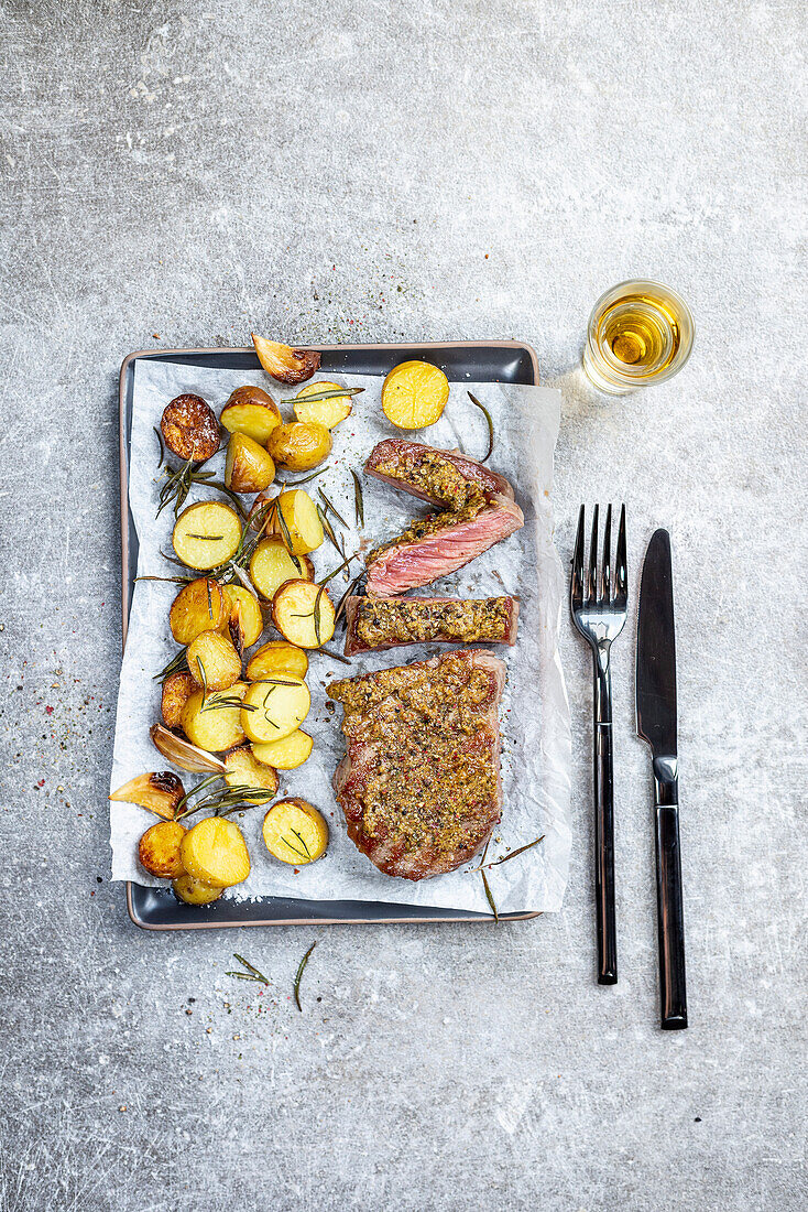 Roast beef with a mustard crust and rosemary potatoes on a baking tray