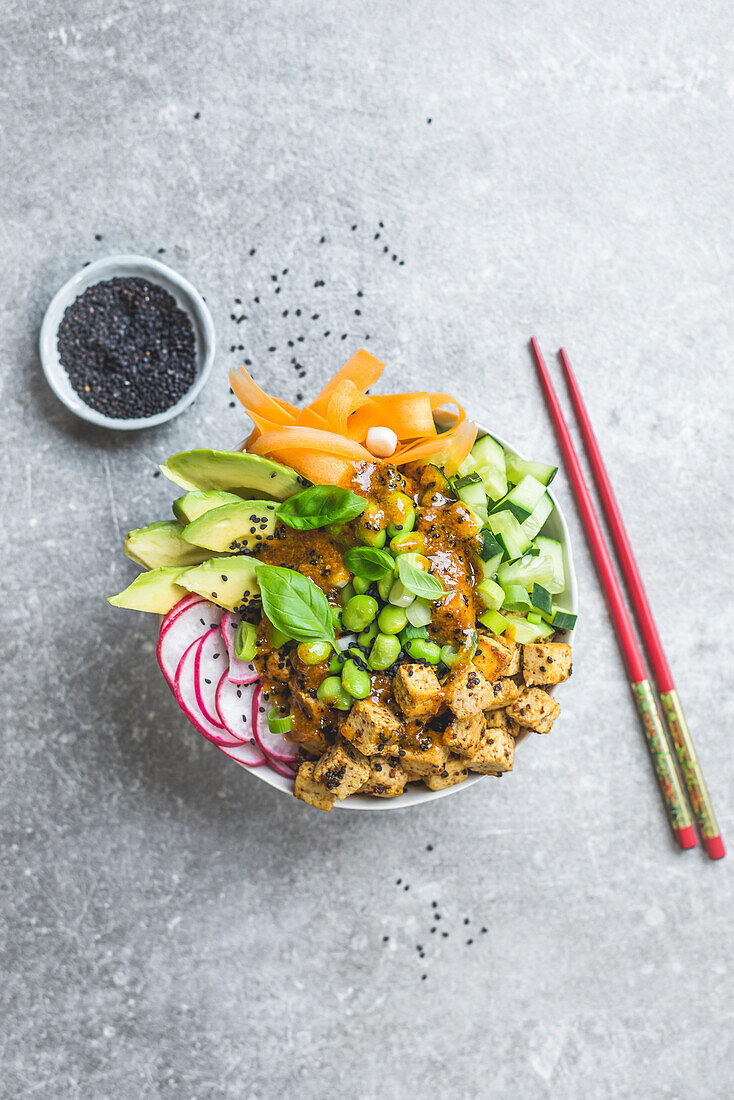 A tofu poke bowl with sesame seeds and chopsticks