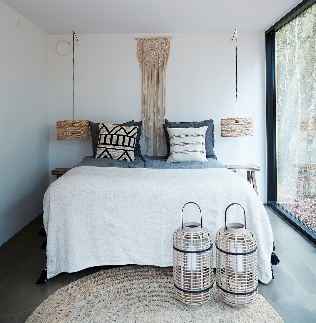 Macramé wall hanging above double bed flanked by reading lamps and with lanterns in the foreground