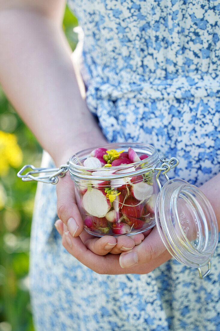 Woman holding preserving jar with radishes and flowers