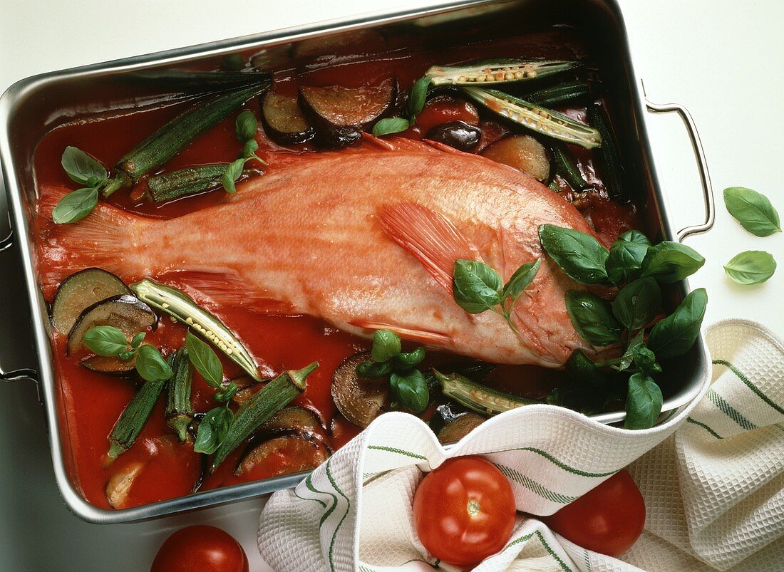 Red perch on tomato sauce with vegetables in cooking dish