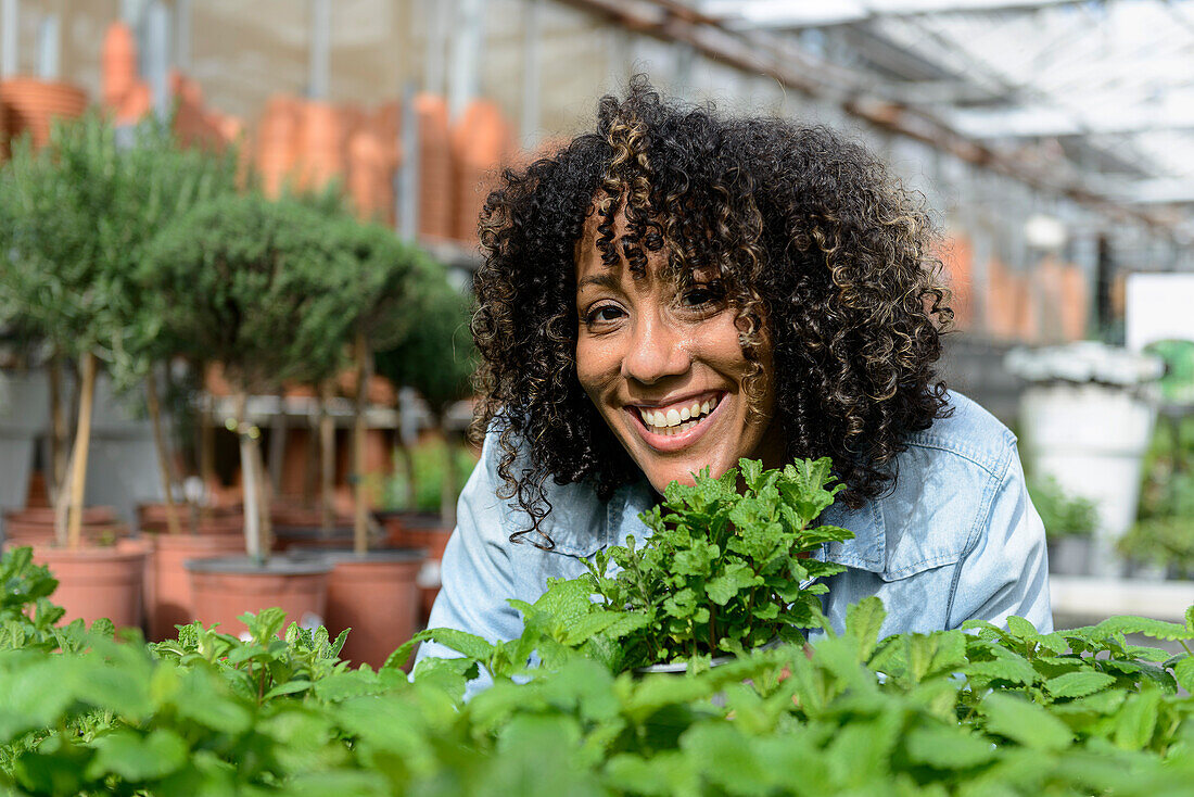 Smiling young woman in nursery smelling herb pot