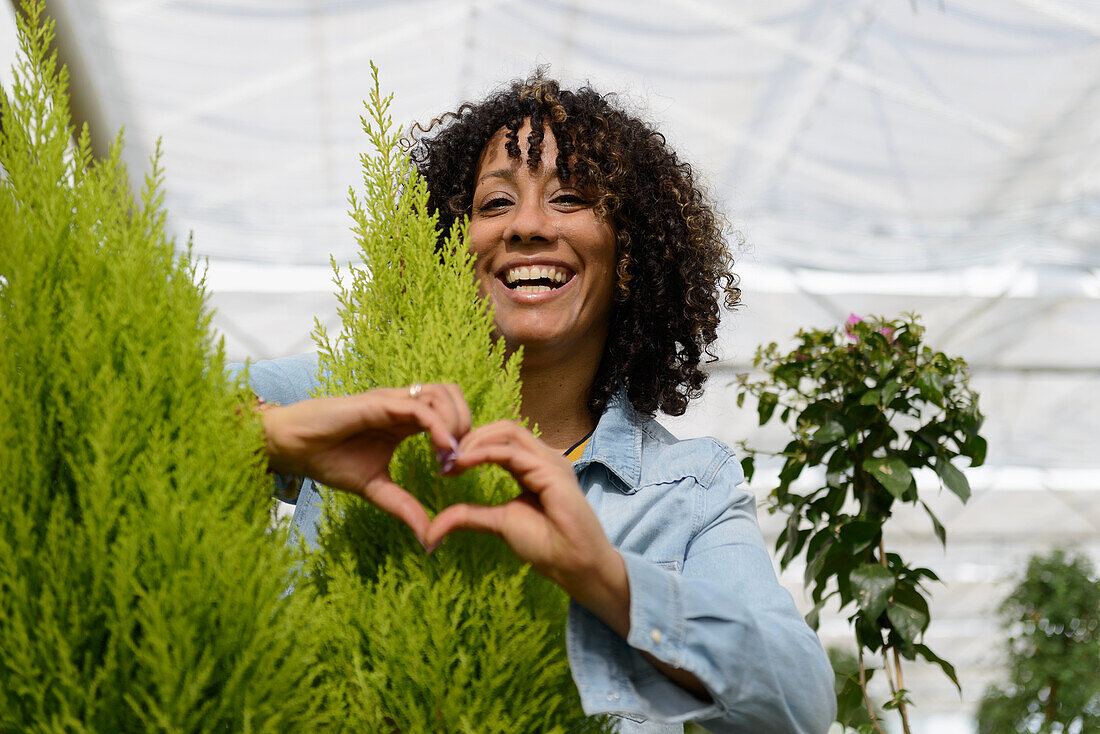 Smiling young woman in nursery forming heart with her hands