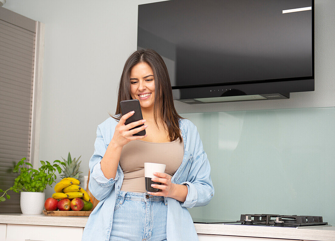 Junge Frau in Küche blickt auf das Smartphone