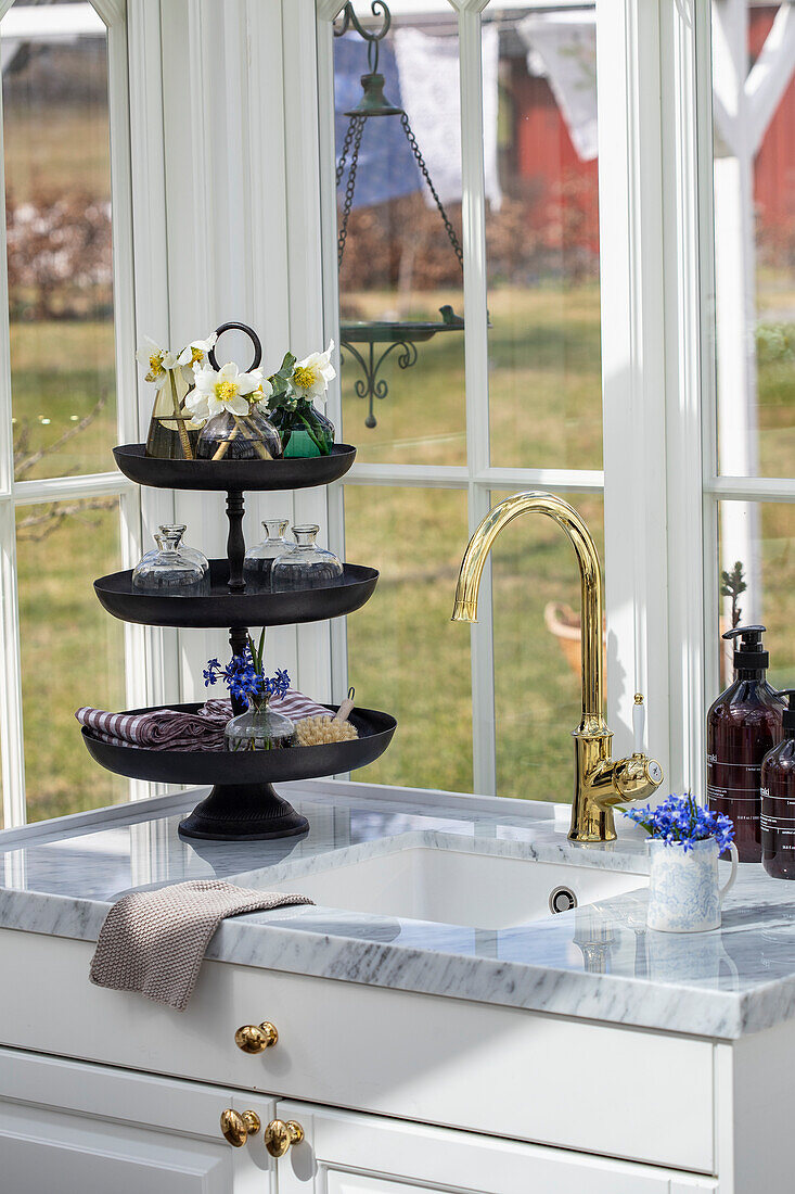 Kitchen sink with golden tap and marble worktop in front of window with garden view