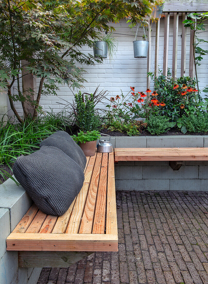 Garten-Sitzbereich mit Holzbänken, dekorativen Pflanzen vor weißer Backsteinwand