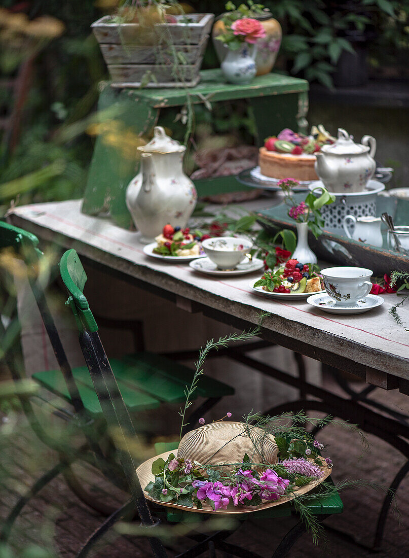 Gedeckter Tisch im Garten mit Teeservice, Kuchen und Blumenarrangement