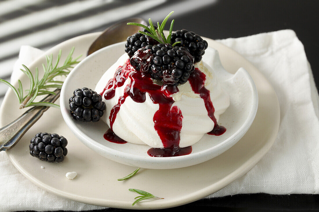 Mini pavlova garnished with blackberries, cream and blackberry sauce