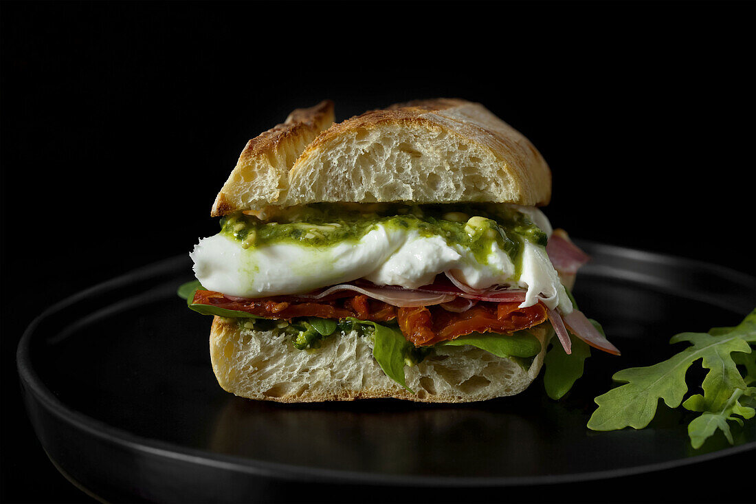 Italian sandwich with rocket salad, sun-dried tomatoes, Parma ham, burrata cheese and pesto