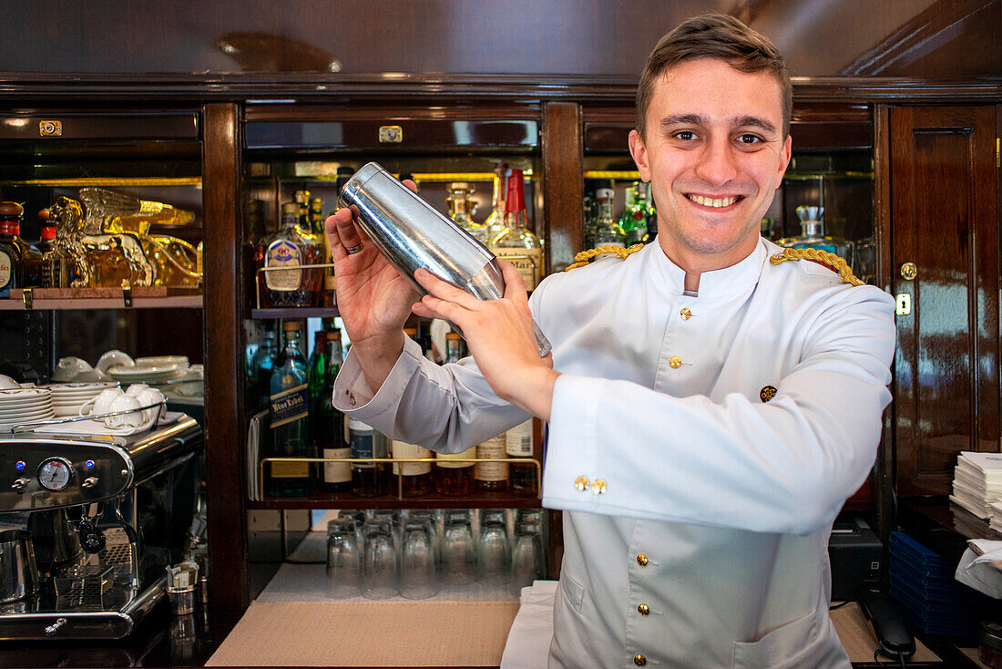 A waiter serves cocktails inside the art deco bar lounge wagon of the train Belmond Venice Simplon Orient Express luxury train.