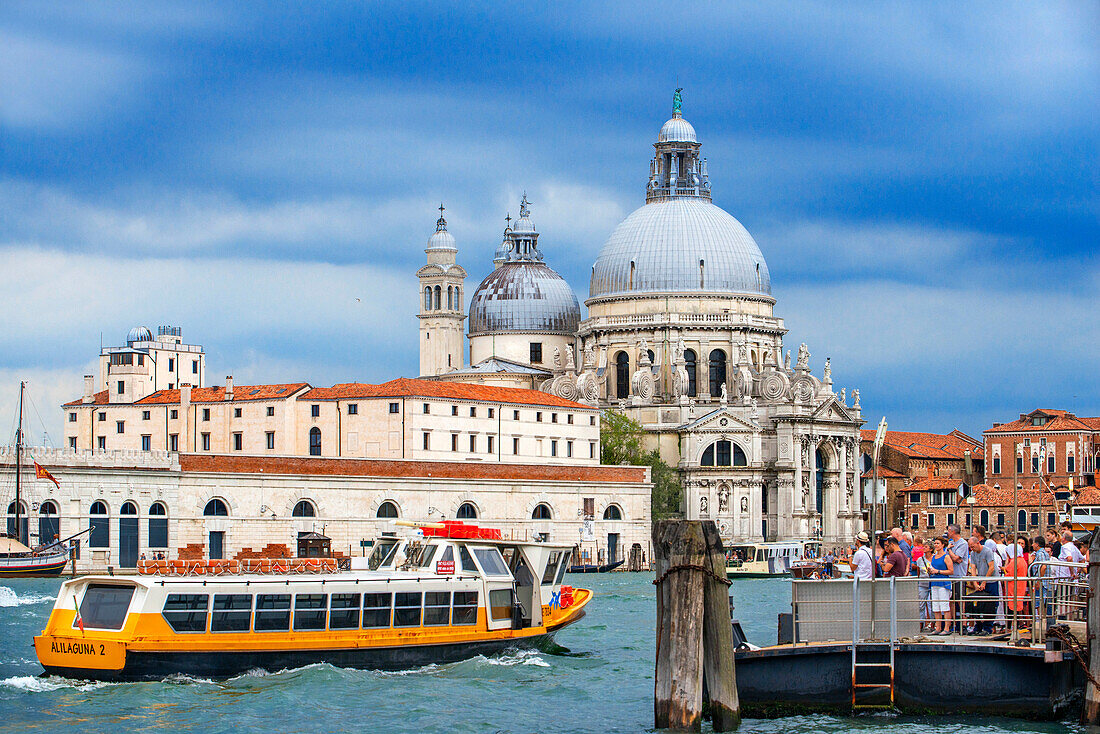 Vaporettos Gondolas, with tourists, on the San Marco gondola stop next to the Basilica de Santa Maria della Salud, Venice, UNESCO, Veneto, Italy, Europe. Cityscape image of Grand Canal in Venice, with Santa Maria della Salute Basilica in the background.