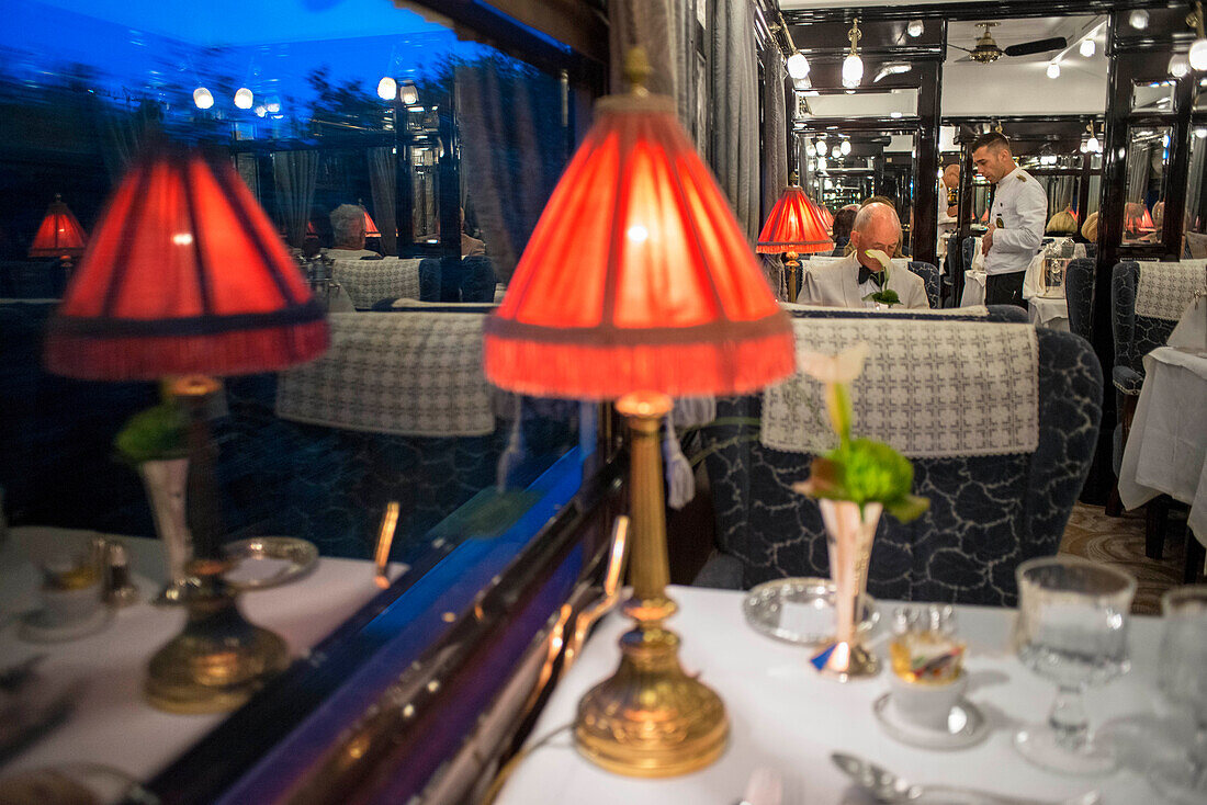 A waiter serves dinner in the art deco restaurant wagon of the train Belmond Venice Simplon Orient Express luxury train.
