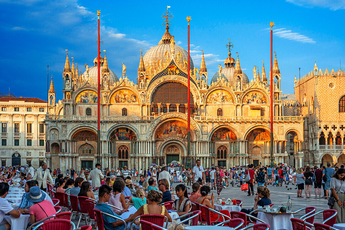 Basilica San Marco reflected in acqua alta in Piazza San Marco at twilight during sunset, Venice, Italy with motion blur on the crowds of tourists