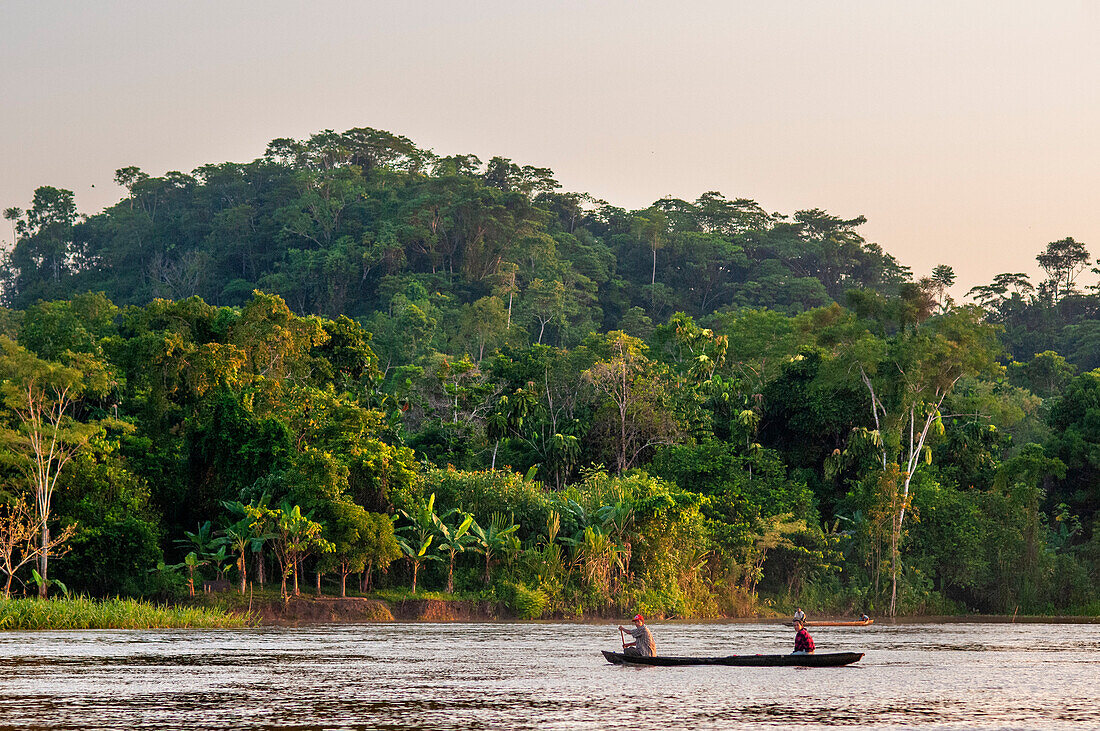 Kleines Holzboot mit Einheimischen auf dem Purus-Fluss im Amazonasgebiet an einem sonnigen Sommertag mit Bäumen am Flussufer, in der Nähe von Iquitos, Loreto, Peru. Fahrt auf einem der Nebenflüsse des Amazonas nach Iquitos, etwa 40 Kilometer von der Stadt Indiana entfernt