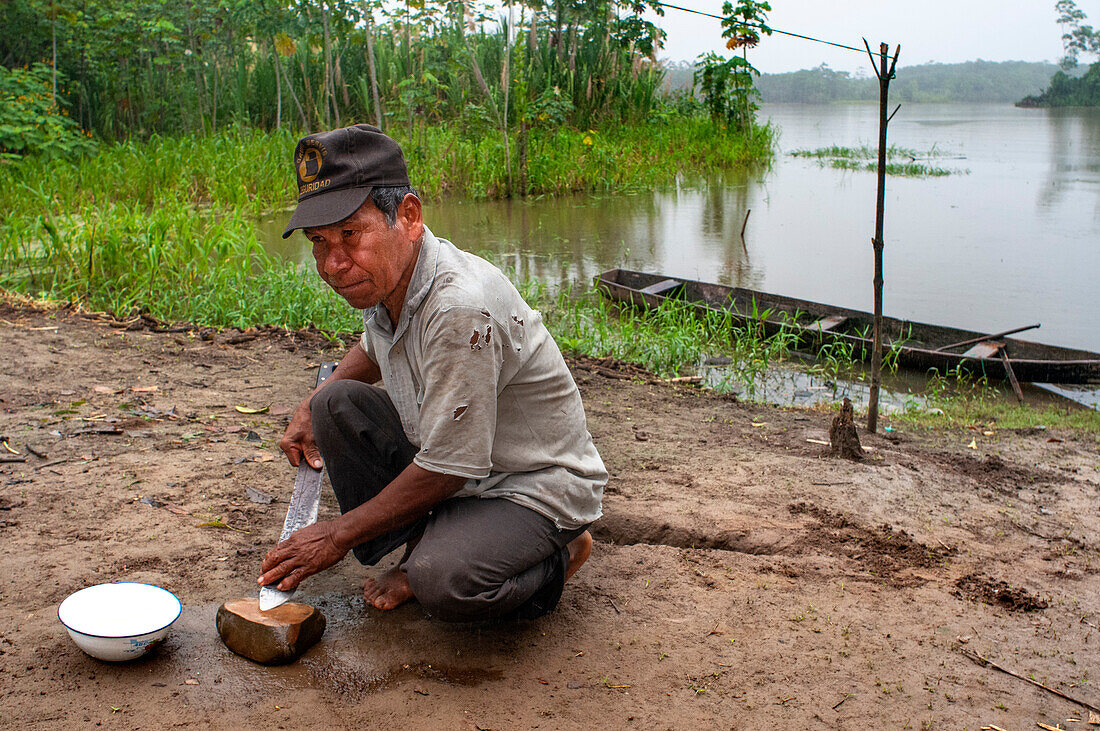 Ein Bewohner des am Fluss gelegenen Dorfes Timicuro I schärft ein Messer vor seinem Haus. Iqutios am peruanischen Amazonas, Loreto, Peru