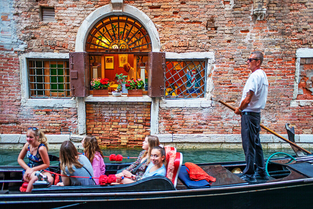 Ein Mann mit einer Gondel fährt an einem Außenrestaurant an einem Kanal in Venedig, Italien, vorbei. Ristorante im Freien in Fondamenta de l'Osmarin, San Marco, Venedig, Italien, an einem Kanal mit Gondeln und Gondoliere