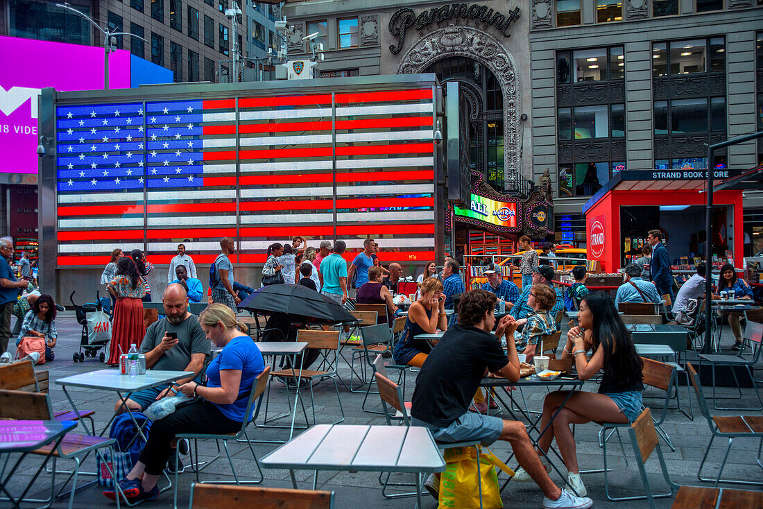 Big american flag in Times Square, New York City at night. Crowds in Times Square on a fall evening, Midtown Manhattan, NY, USA