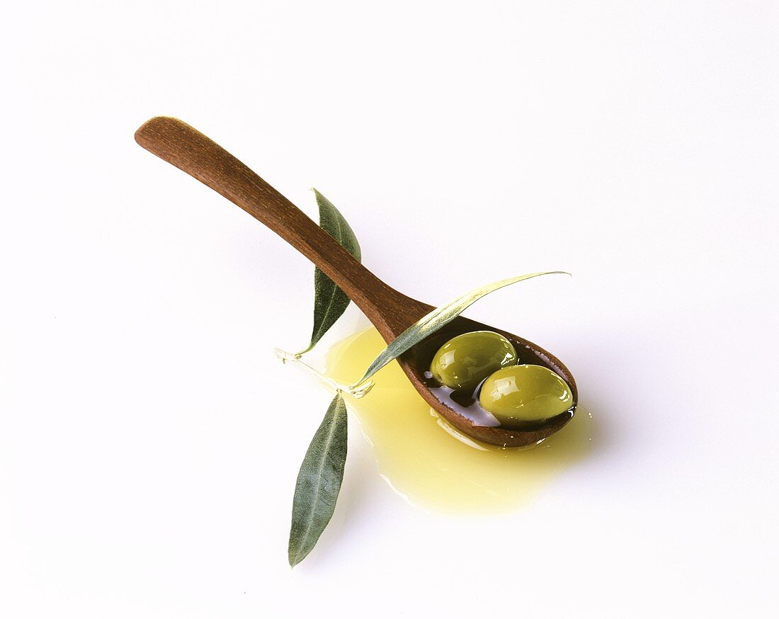 Two green olives with olive oil on wooden spoon & olive leaves