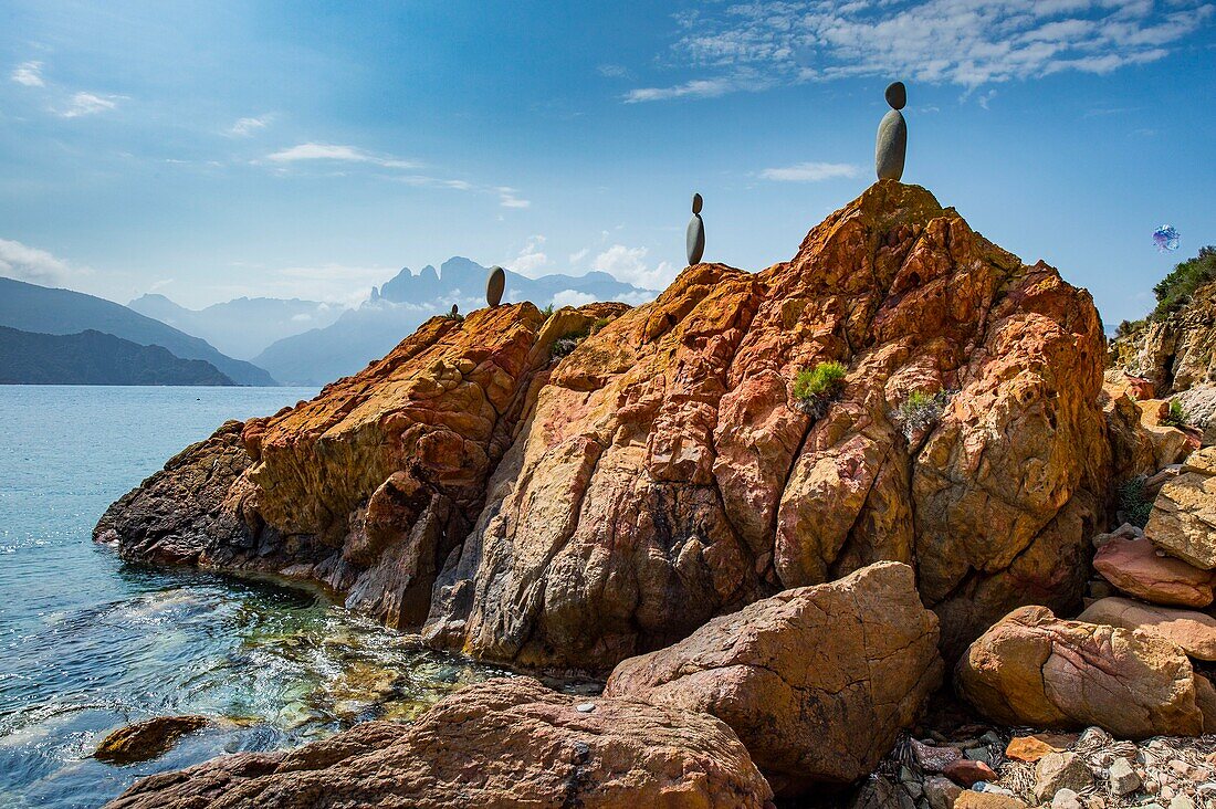 France, Corse du Sud, Porto, Gulf of Porto listed as World Heritage by UNESCO, on the beach Gradelle, an artist has stacked large gray pebbles to form ephemeral statues that stand out on the ocher rocks, a marvel
