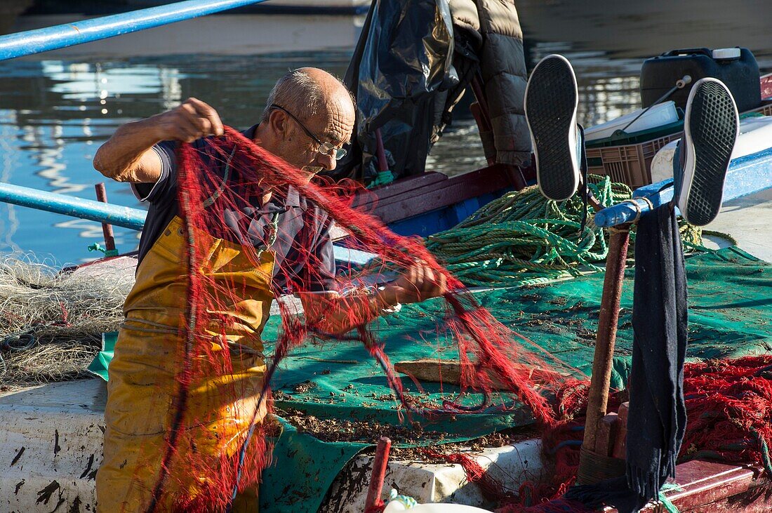 France, Corse du Sud, Ajaccio, a fisherman cleans his nets on one of the many colorful boats in the port Tino Rossi,