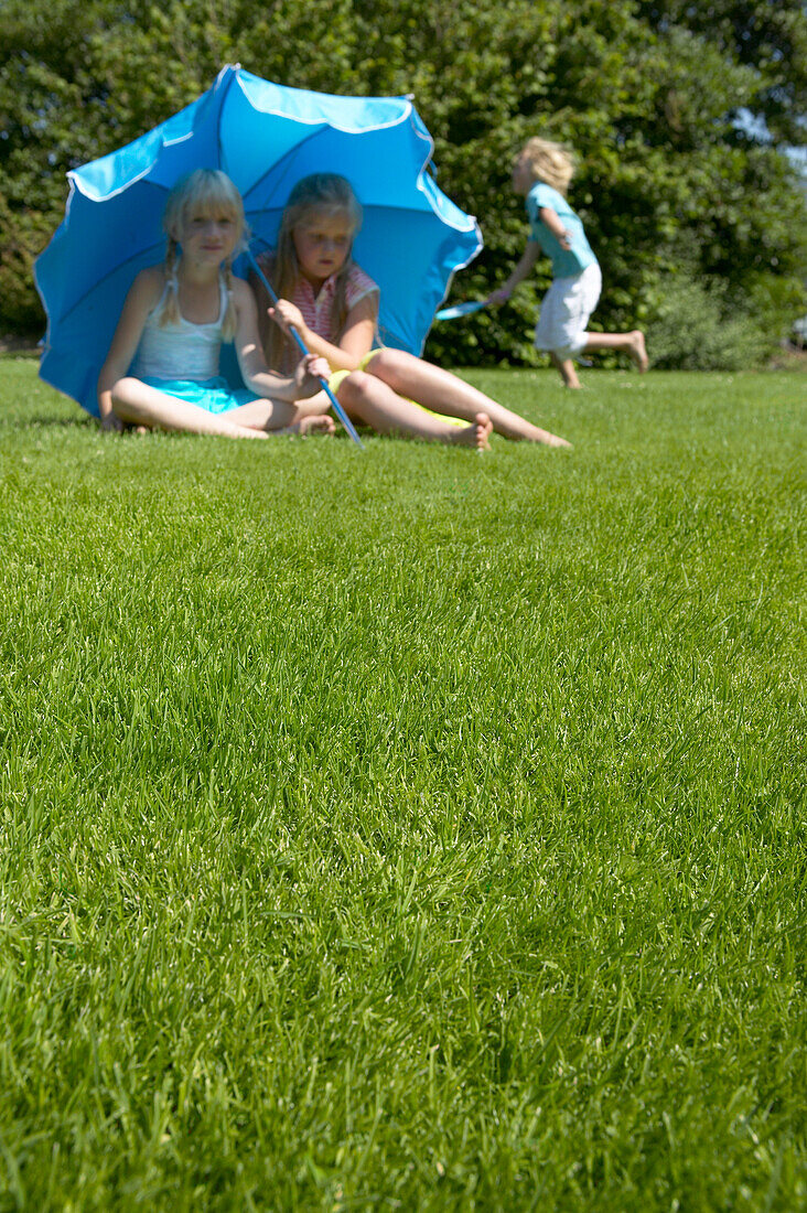 Mädchen mit blauem Schirm auf dem Rasen sitzend