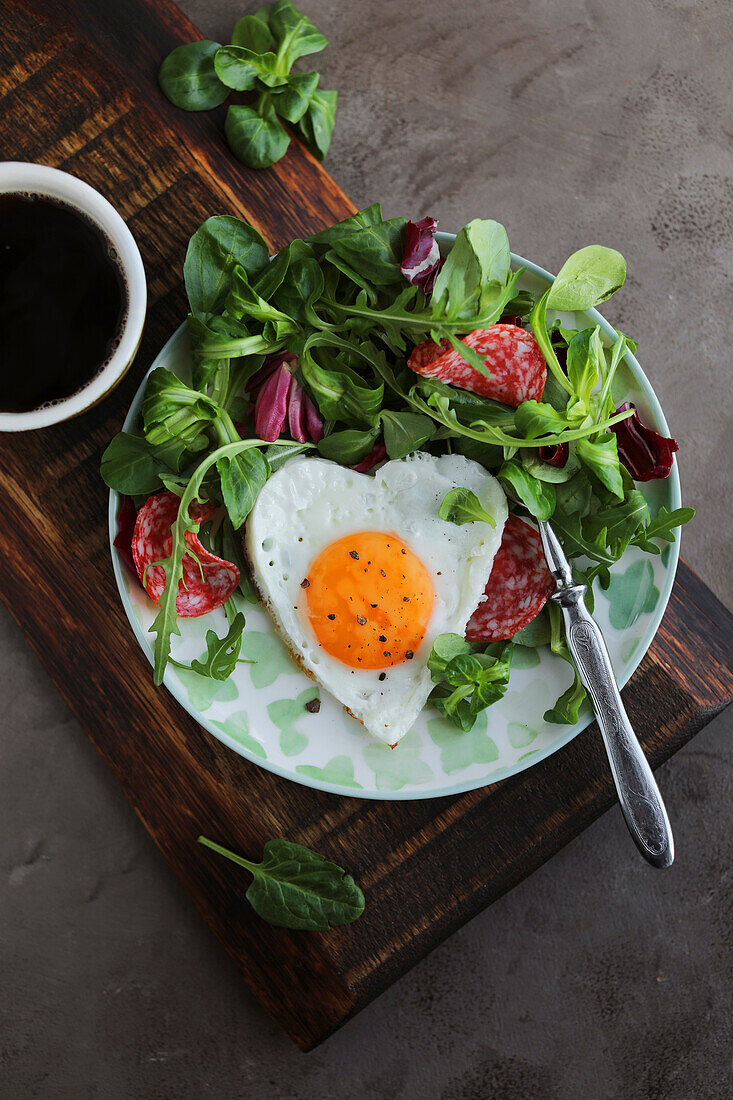 Heart-shaped fried egg with salami and salad