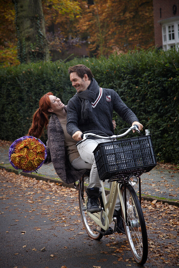 Couple riding bicycle holding flowers