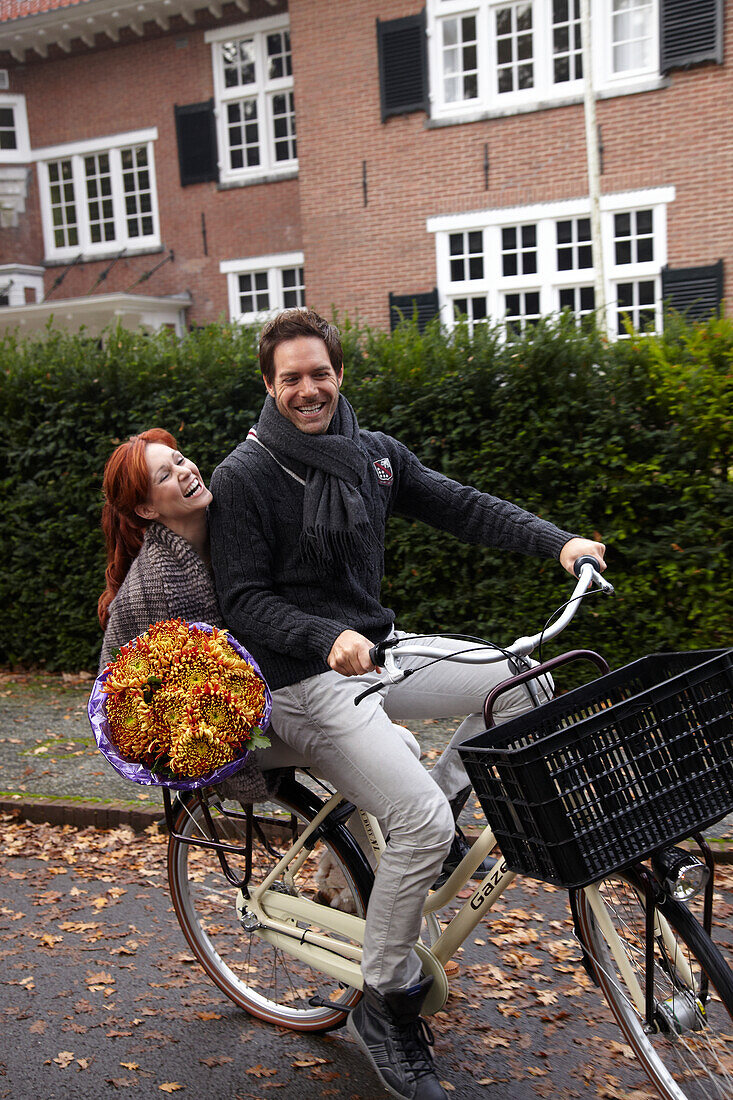 Couple riding bicycle holding flowers