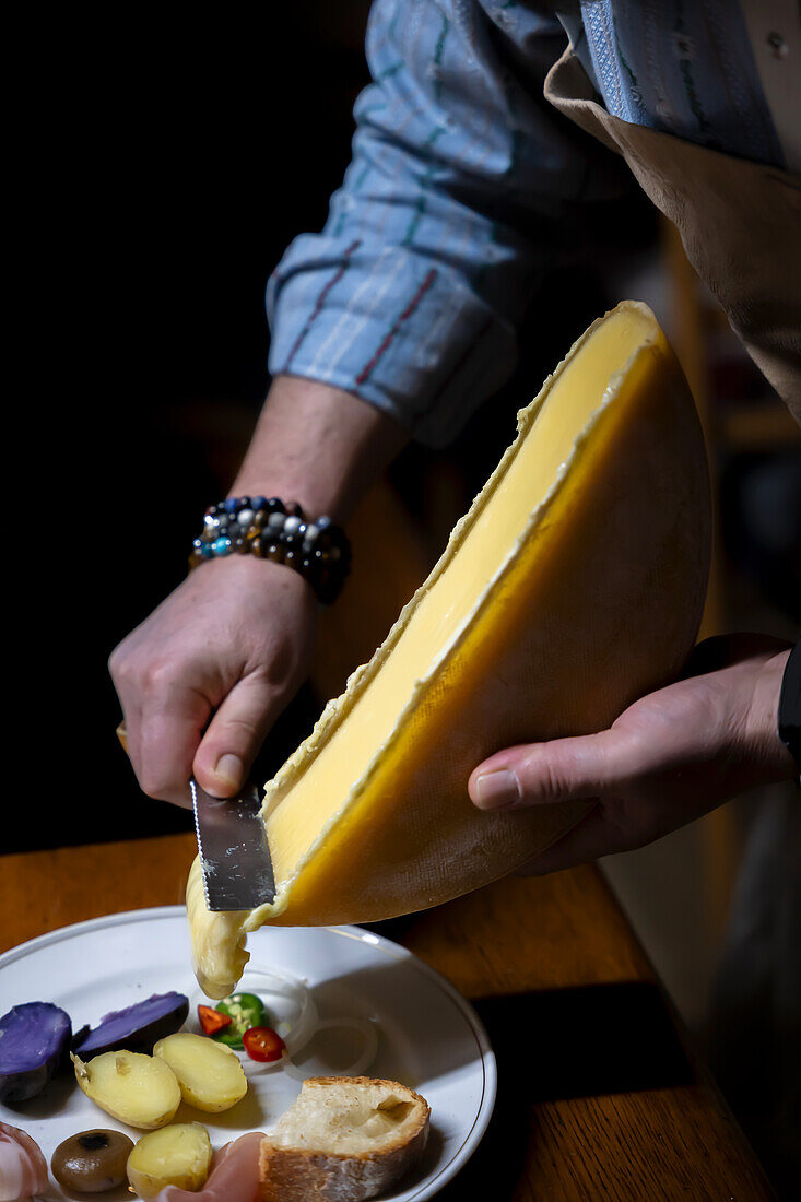 Man scrapes melted, traditional Swiss raclette cheese onto plate