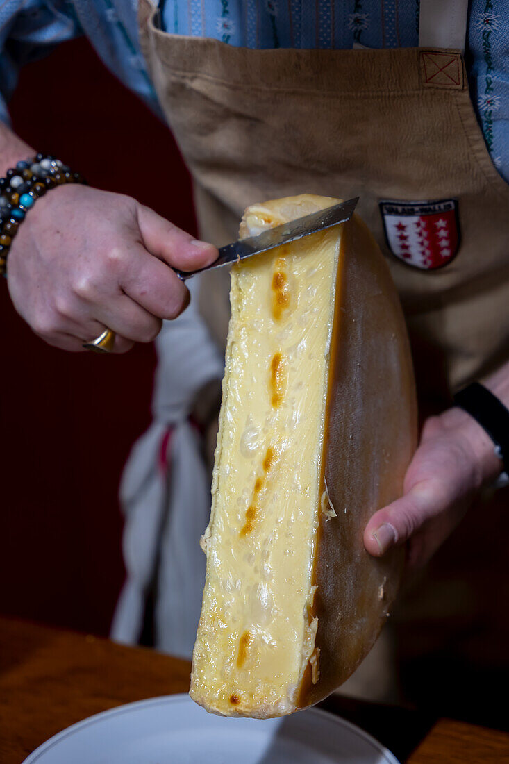Man scrapes melted, traditional Swiss raclette cheese onto plate