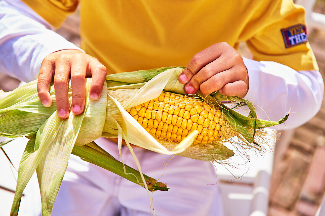 Junge schält Maiskolben