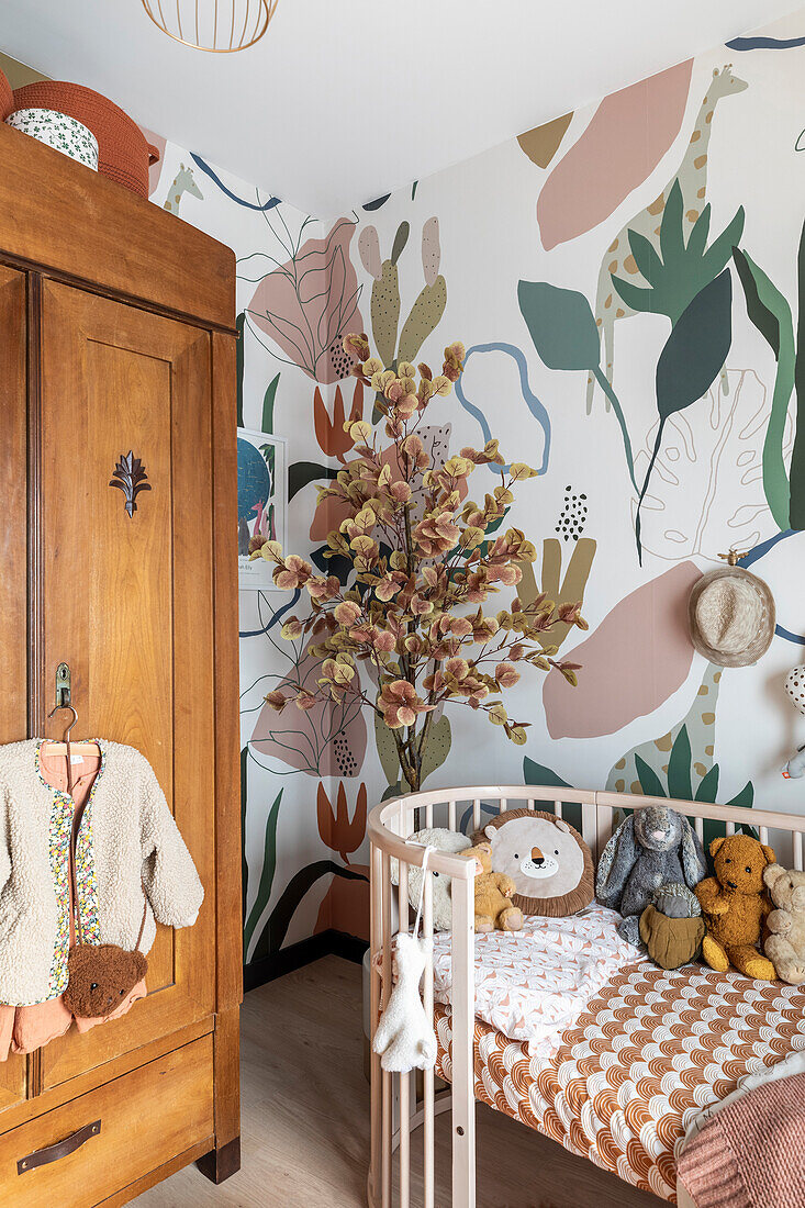 Babyzimmer mit hölzernem Kleiderschrank, floral gemusterter Tapete und Dekobaum