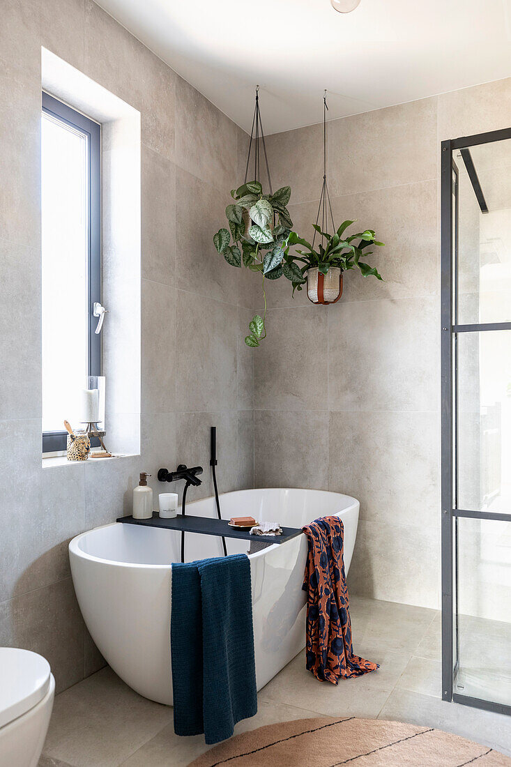 Freestanding bathtub with hanging plants and colourful towels in a modern bathroom