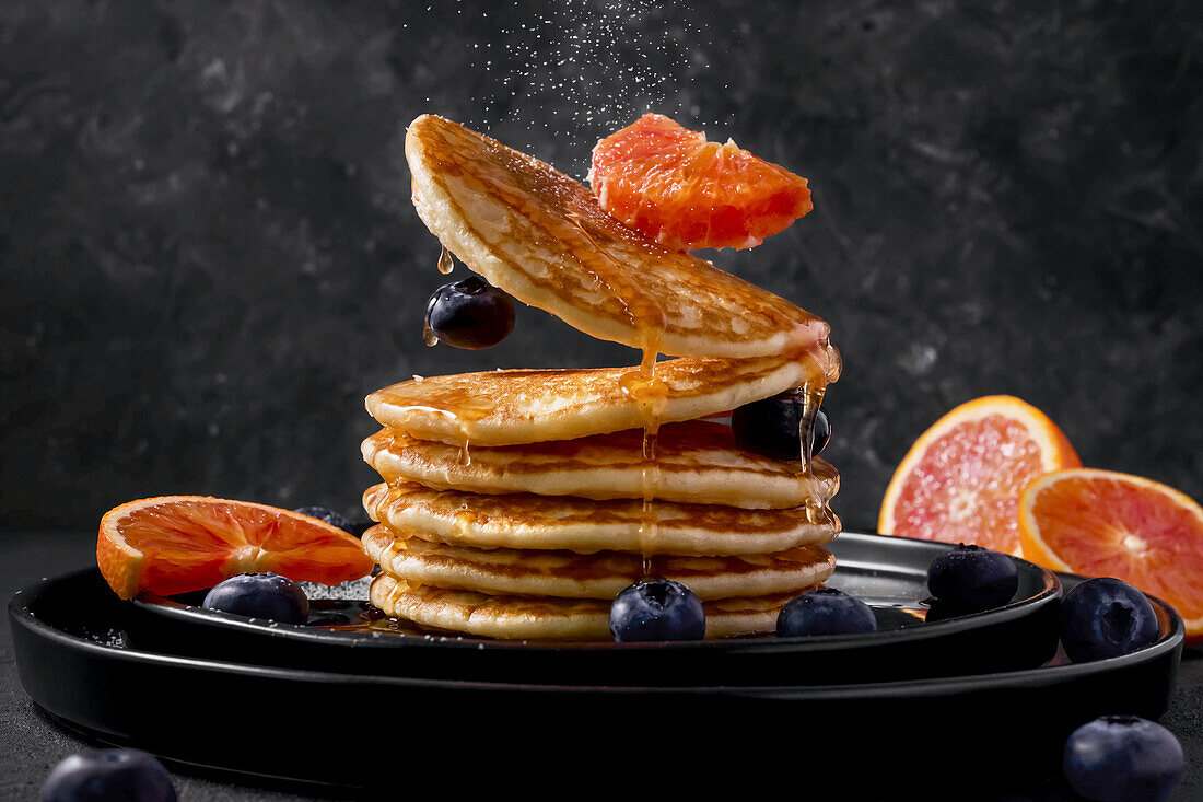 A stack of pancakes with maple syrup, blueberries and blood oranges