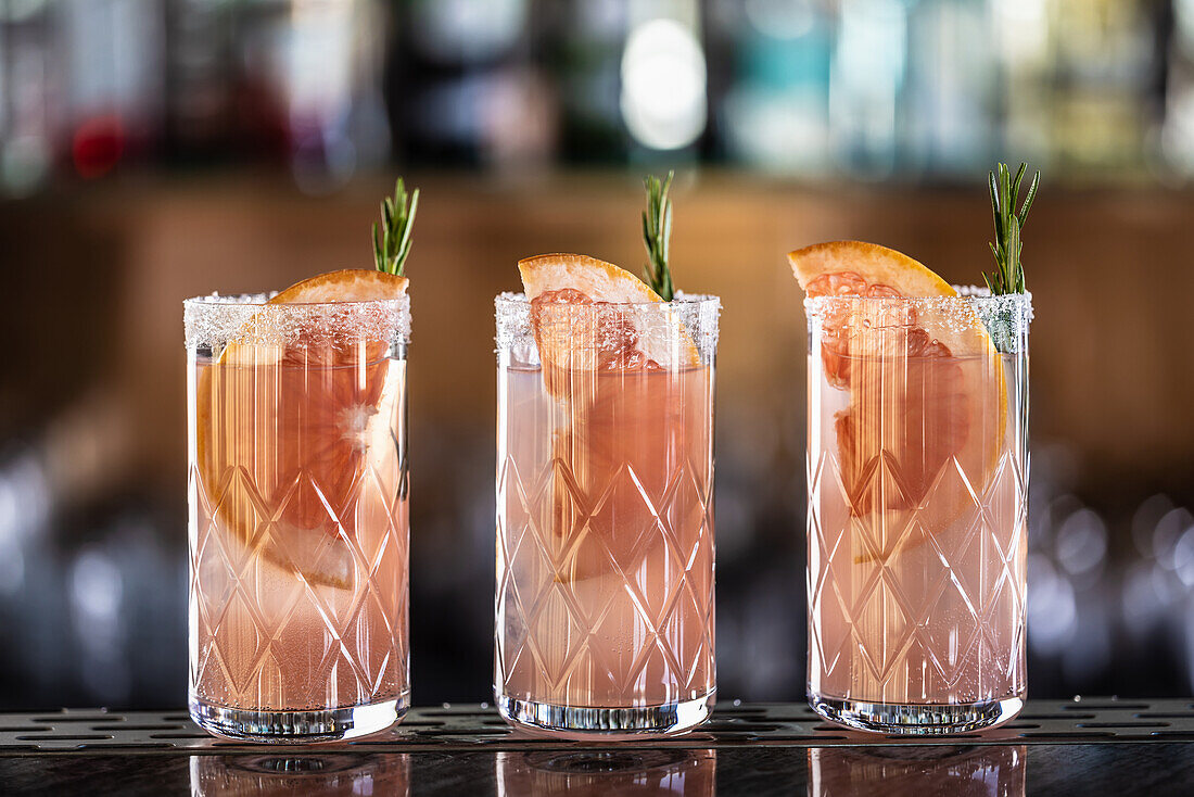 Three Paloma cocktails, garnished with grapefruit and rosemary