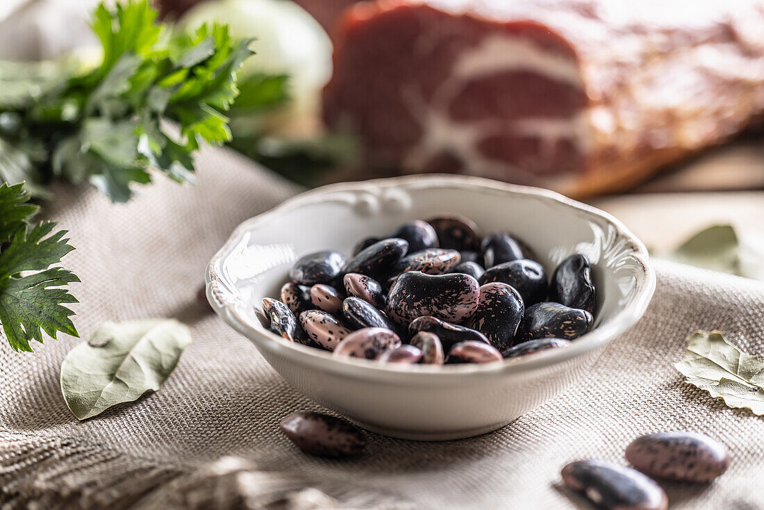 Käferbohnen in Schüssel und geräucherter Schweinenacken im Hintergrund