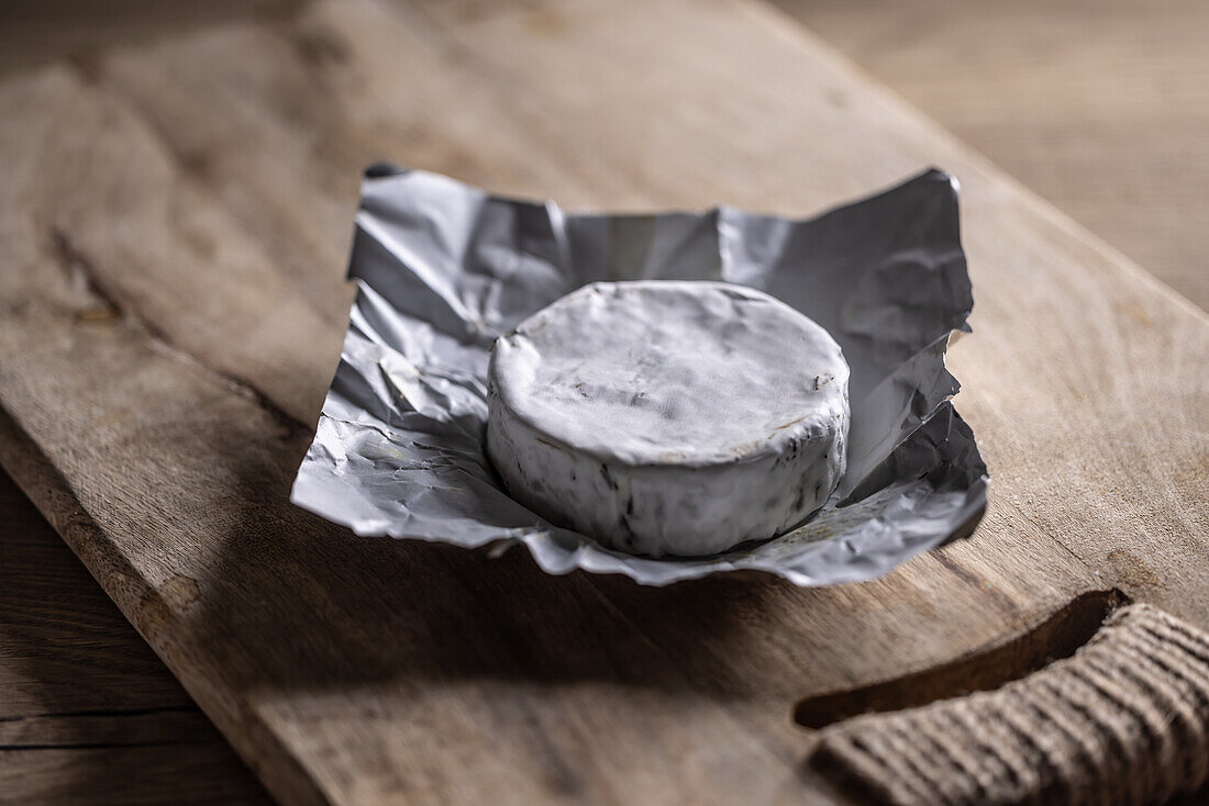 Brie cheese in aluminium foil on a wooden cutting board