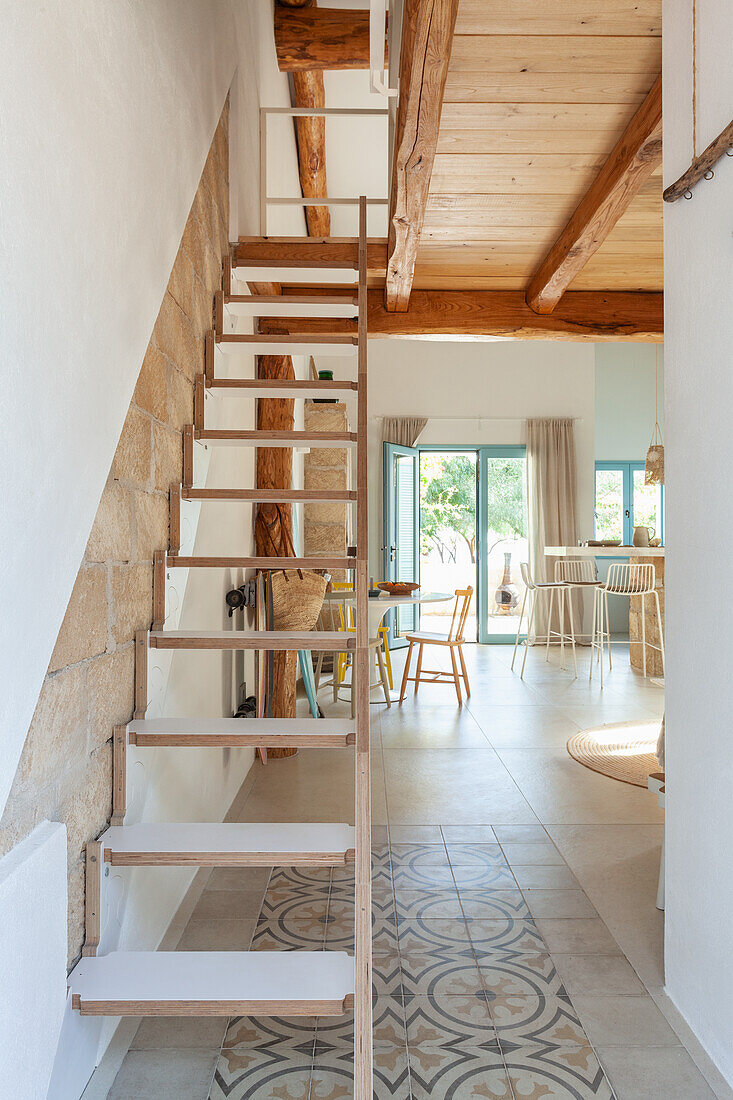 Ausklappbare Holztreppe in modernem Wohnraum mit gemustertem Fliesenboden und Holzbalkendecke