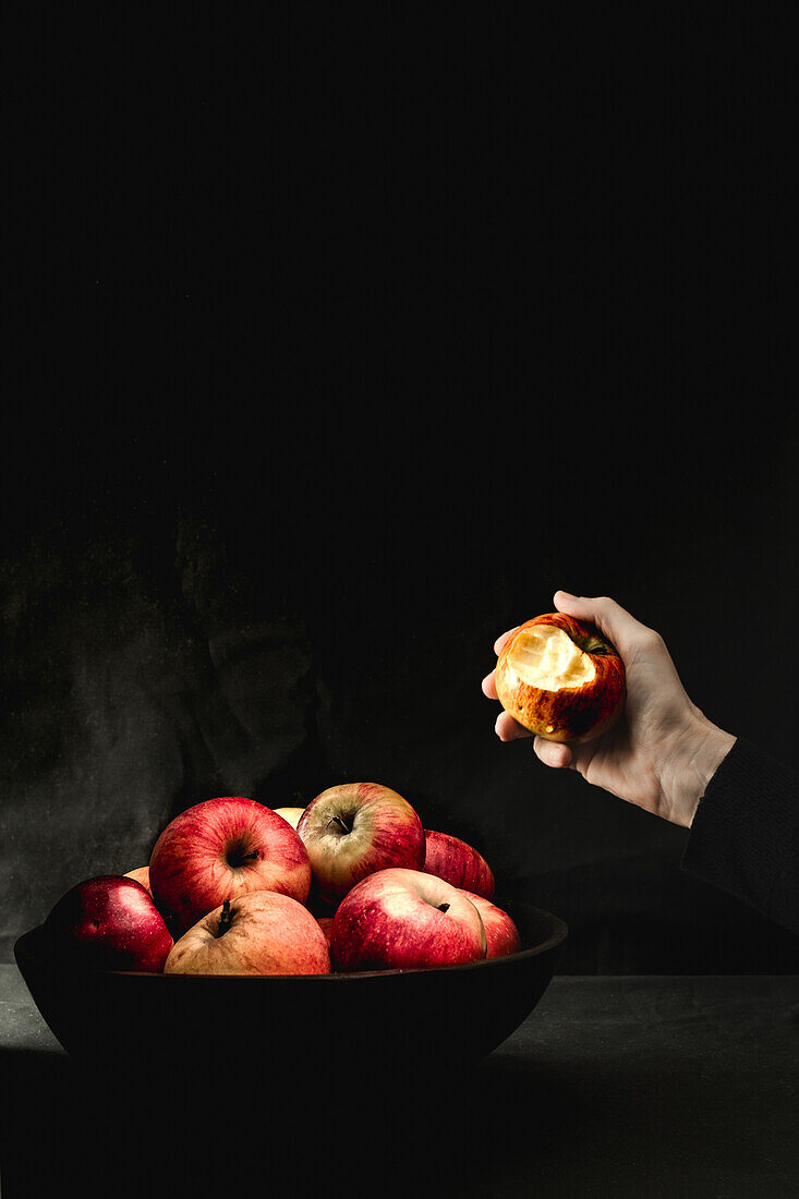 Hand nimmt roten Apfel aus einer schwarzen Schüssel mit Äpfeln