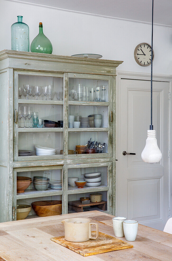 Display cabinet with crockery and glasses, wooden table and wall clock