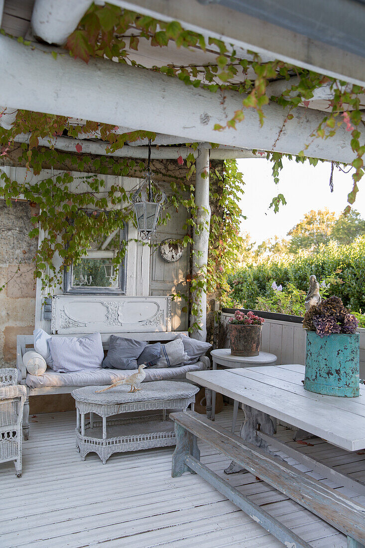 Überdachte Terrasse mit Vintage- und Rattanmöbeln und Pflanzenranken