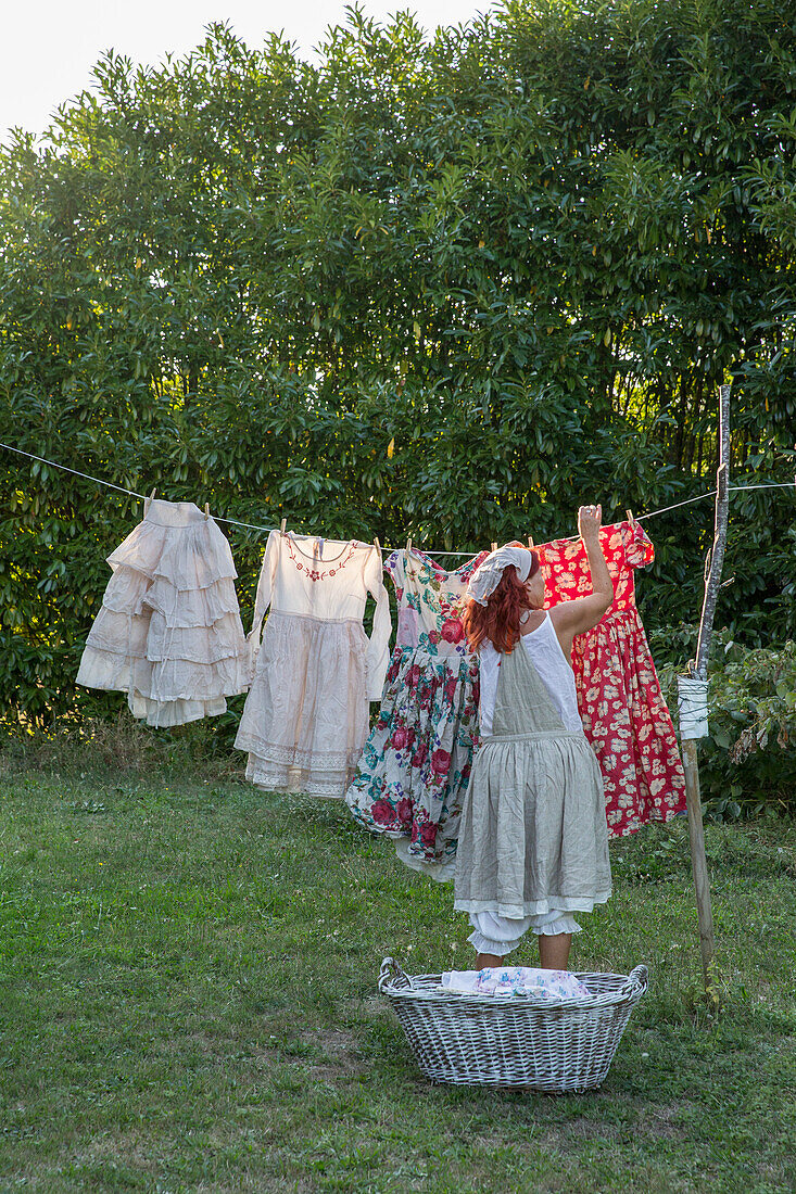 Frau hängt bunte Sommerkleider auf Wäscheleine im Garten auf