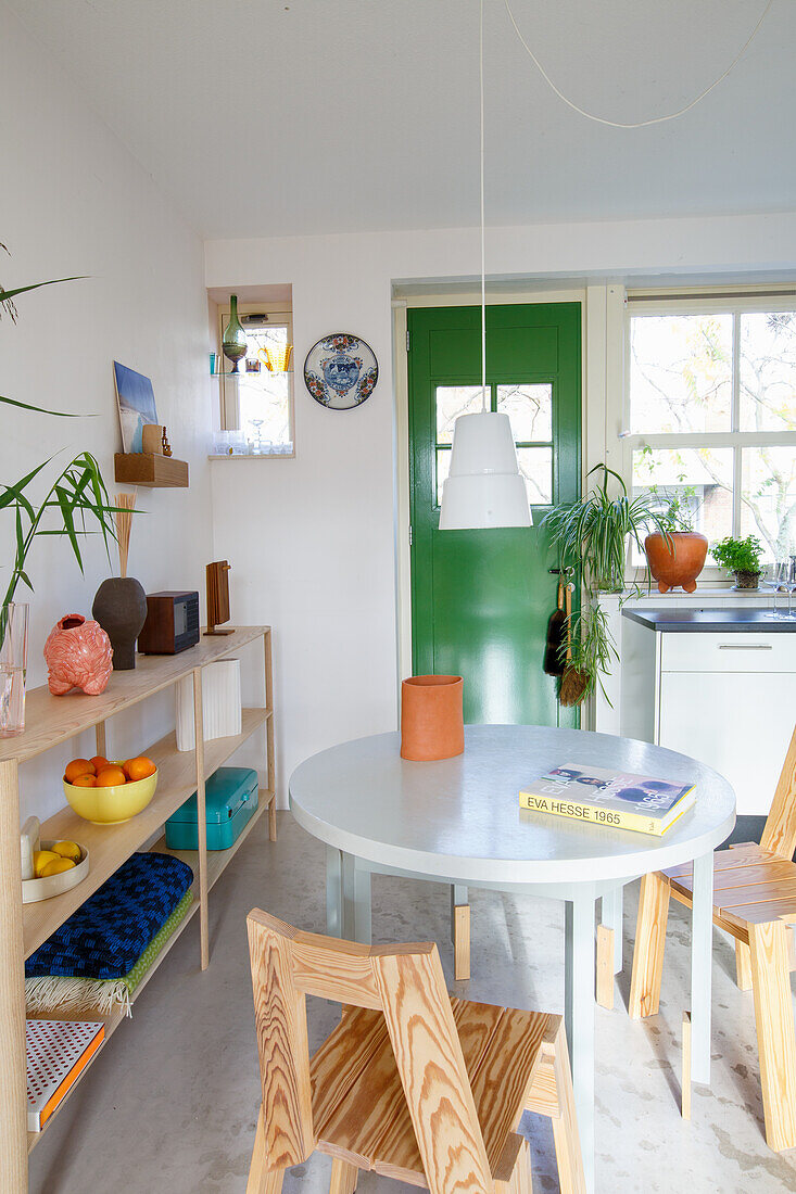 Round dining table with wooden chairs in a light-coloured kitchen with a green door