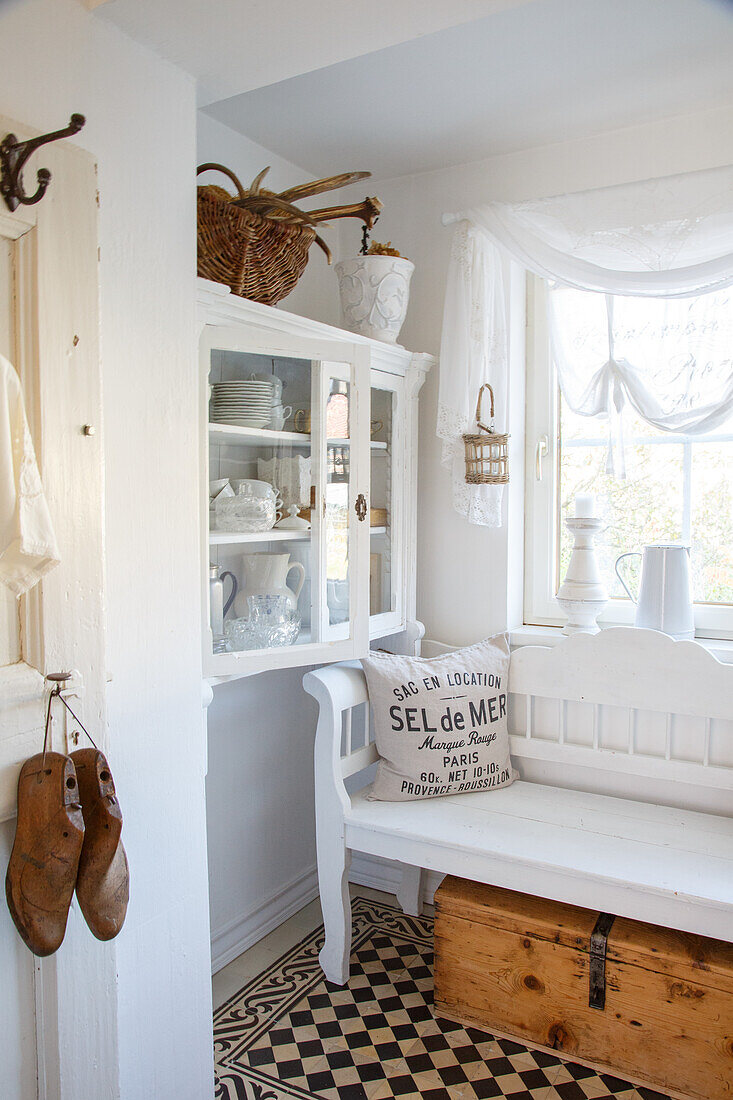 Sitting area with white wooden bench, tiled floor and wooden chest as storage space