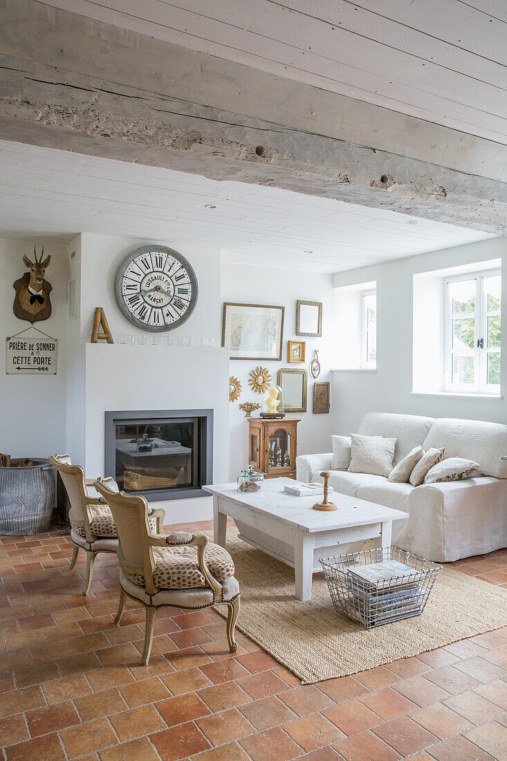 Living room in rustic country house style with terracotta tiles, white sofa and fireplace