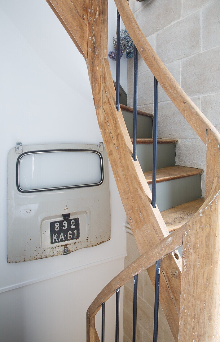 Holz-Wendeltreppe mit Metallgeländer und alter Autotür als Dekoration im Treppenhaus