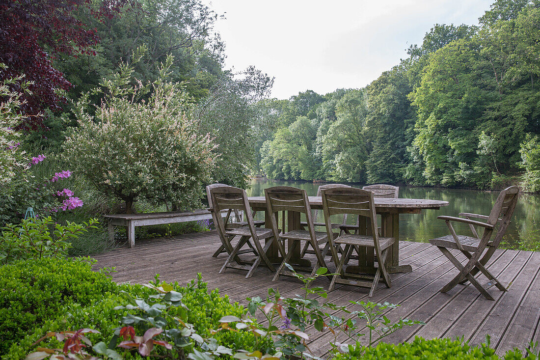 Holzterrasse mit Gartentisch und Stühlen mit Blick auf Fluss und bewaldete Uferbereiche