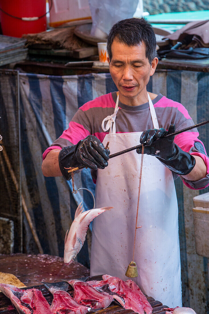 Ein Mann wiegt in einem Laden auf der Straße in Hongkong, China, Fisch für den Verkauf