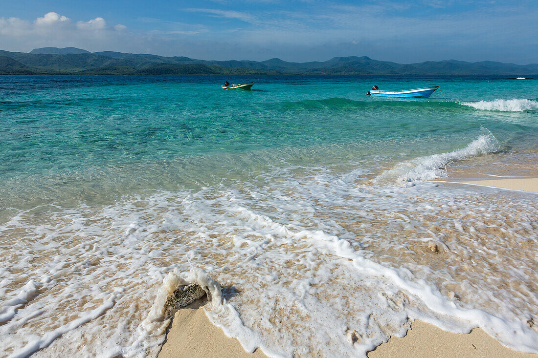 Motorboote liegen im klaren, flachen Wasser um Cayo Arena oder die Paradiesinsel vor Anker. Dahinter liegt der Nationalpark Monte Cristi in der Dominikanischen Republik, Hispaniola.